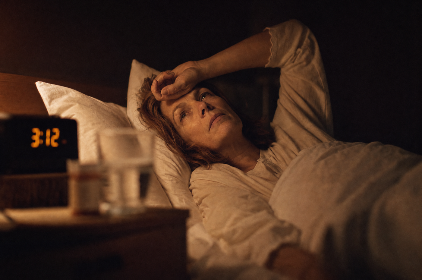A woman awake in the middle of the night, looking at the ceiling as the bedside clock reads 3:12 AM