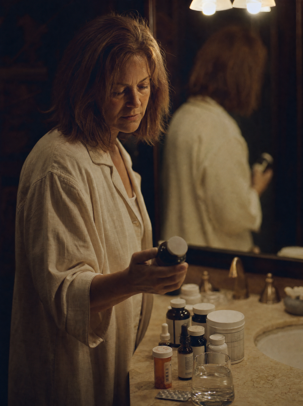 A woman standing at the bathroom counter at night surrounded by melatonin bottles and pill packets